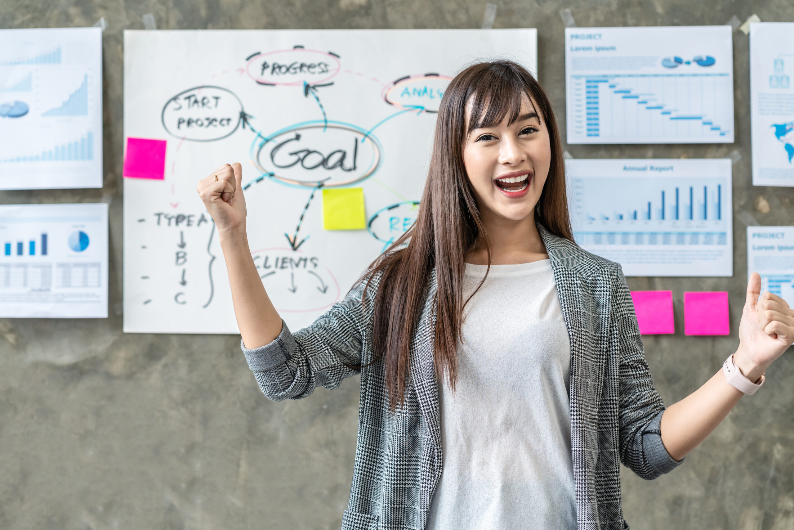 Portrait of happy woman standing and cheerful in office workplace with document plan and goal on wall background.