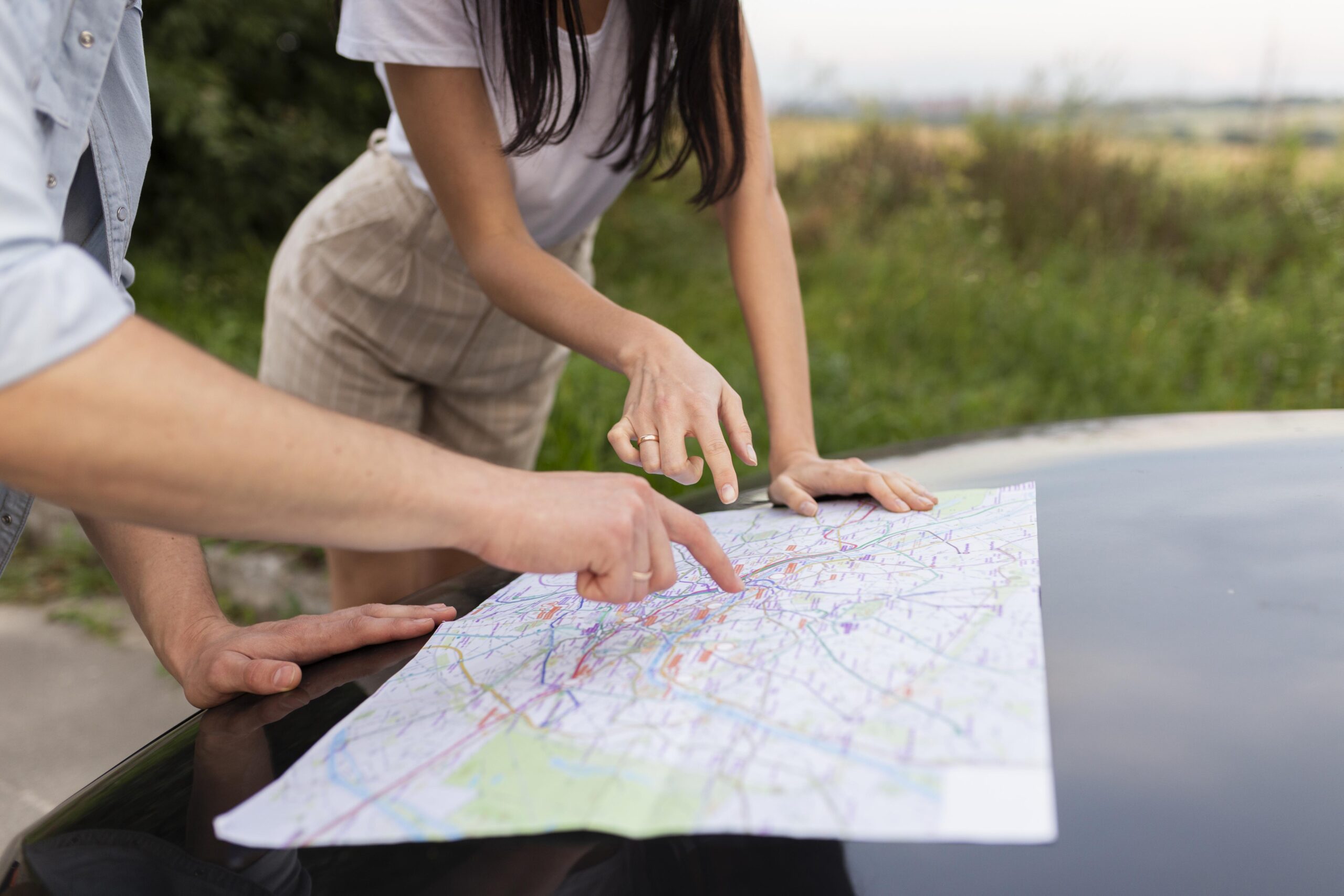 Two people pointing at a paper map on a car hood.